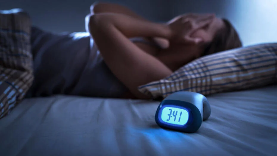 Person lying awake in bed at night, hands on neck, with a digital alarm clock showing 3:41 a.m.